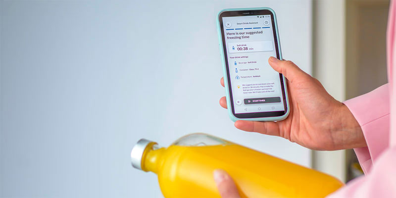 Απεικονίζεται άτομο να κρατάει κινητό με ανοιχτή την εφαρμογή και ένα μπουκάλι.