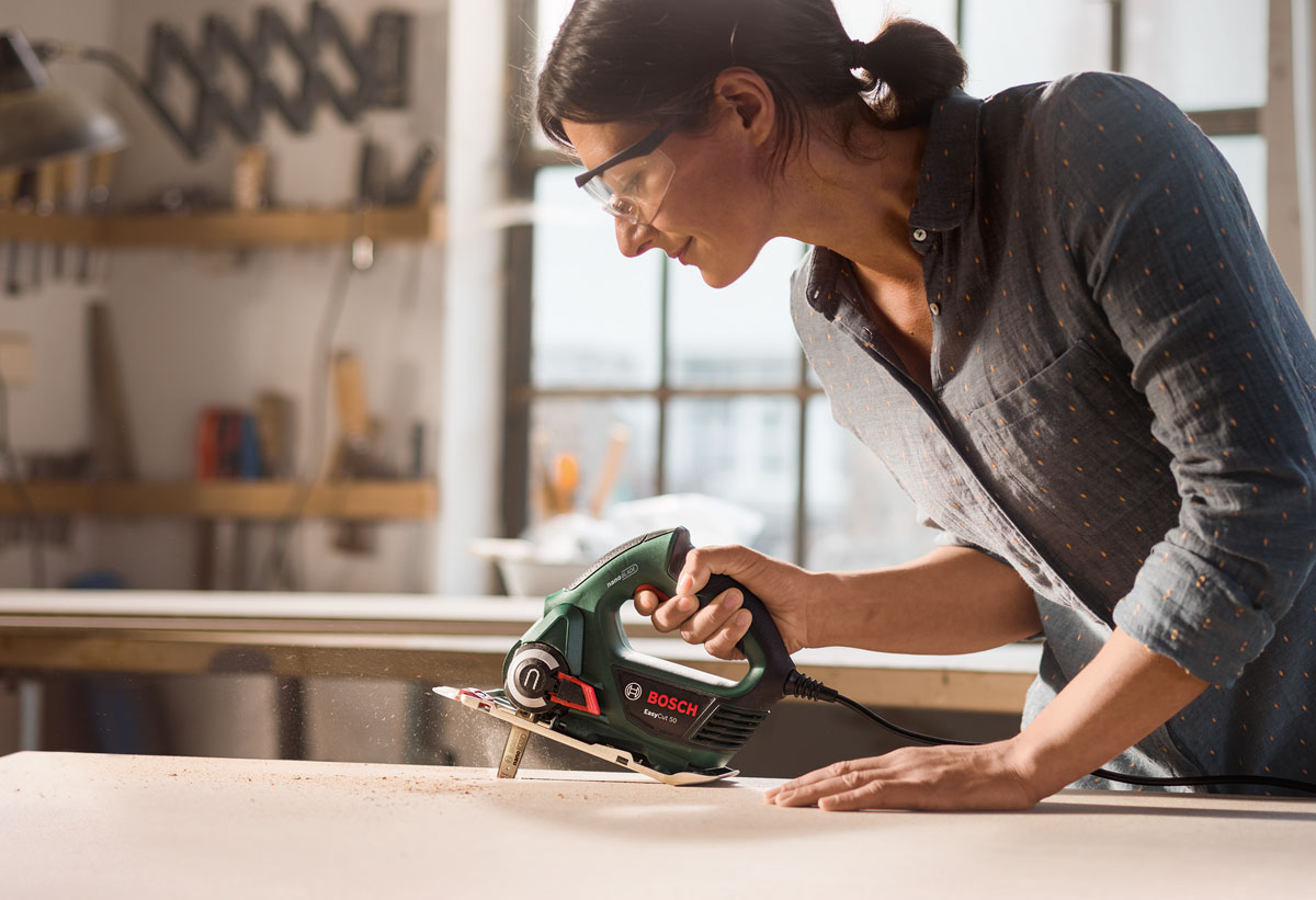 Μία γυναίκα χρησιμοποιεί τη σέγα Bosch EasyCut 50 για να κόψει ξύλο.