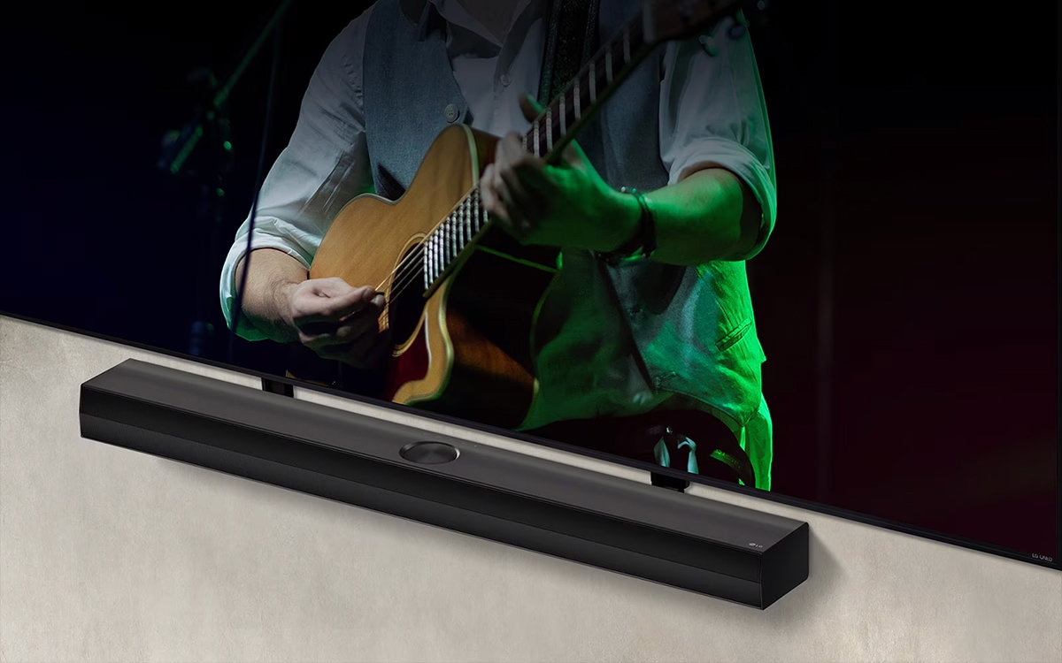 LG Soundbar μπροστά από μαύρο φόντο αποκαλύπτει τη σχεδίασή στην αριστερή γωνία και απομακρύνεται για να δείξει όλο το soundbar. Μια LG QNED TV εμφανίζεται με τον βραχίονα Synergy. Το Soundbar βρίσκεται πάνω στον βραχίονα Synergy, ακουμπά στον τοίχο με την κάτω οθόνη της τηλεόρασης ορατή, δείχνοντας έναν άντρα να παίζει κιθάρα.